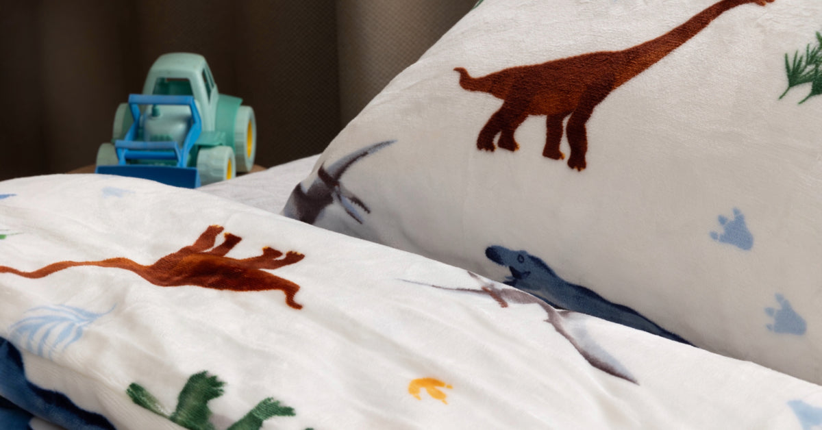 Een dichtbijfoto van een zacht, velvet dekbedovertrek met dino-print, prachtig opgemaakt op een bed in een gezellige kamer. Op de tafel naast het bed staat een schattig autootje, wat de speelse sfeer van de kamer versterkt.
foto: dekbedovertrek 140x200 dino.
