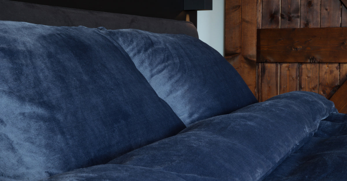 Een blauw velvet dekbedovertrek met een subtiele glans, netjes opgemaakt op een bed. De fluweelzachte stof en diepe kleur geven het slaapkamerinterieur een luxe en comfortabele uitstraling. Foto: dekbedovertrek blauw.