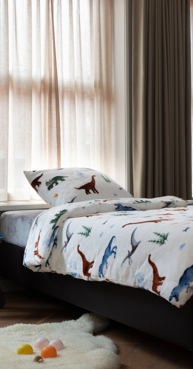 Dekbedovertrek van zachte velvet stof met een vrolijke dino-print, op een bed in een kinderkamer. De kleurrijke en speelse ontwerpen creëren een gezellige sfeer, perfect voor een avontuurlijke slaapomgeving voor kinderen. foto: dekbedovertrek kinderen.