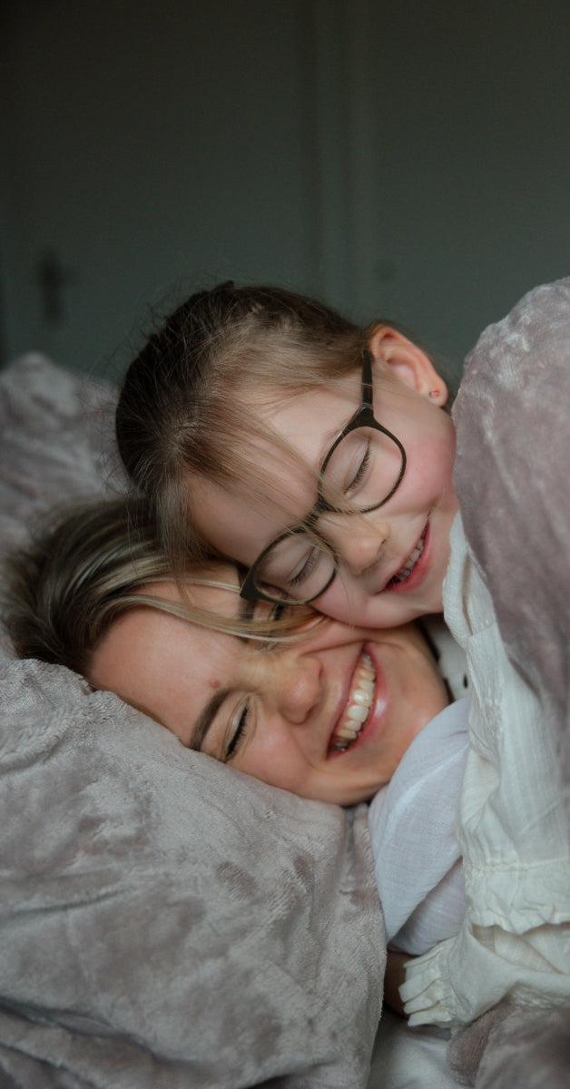 Moeder en dochter delen een bijzonder moment onder een luxe taupe velvet dekbedovertrek. Het warme materiaal omarmt hen terwijl ze samen lachen en genieten van deze knusse, liefdevolle sfeer in hun huis. Een herinnering om te koesteren! foto: dekbedovertrek moeder met dochter.