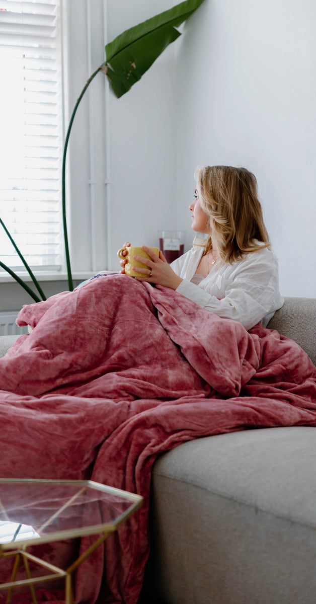 Roze velvet dekbedovertrek met een zachte, fluweelachtige stof, gewikkeld om een meisje dat op een bank in een kamer zit. De stof straalt warmte en luxe uit, terwijl de roze kleur een gezellige sfeer toevoegt. foto: dekbedovertrek op de bank.