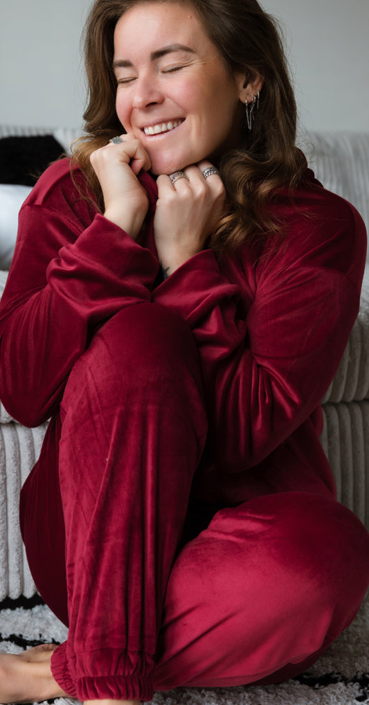 Lisa zit op de grond, genietend van het comfort van haar zachte, rode huispak. Haar ogen zijn gesloten en haar gezicht straalt ontspanning uit terwijl ze de warme, comfortabele stof om haar heen voelt.
foto: huispak rood met Lisa