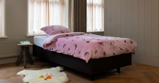 Een peuterbed opgemaakt met een velvet dekbedovertrek, versierd met kleurrijke vlinders. Het bed staat in een gezellige kinderkamer, met zachte stoffen en warme kleuren voor een knusse uitstraling. foto: peuter dekbedovertrek vlinder.